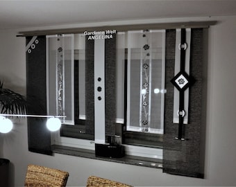 Può includere: Un set di tende a pannello con pannelli testurizzati grigio scuro alternati a pannelli bianchi trasparenti con ricami floreali. Il design include una striscia verticale bianca centrale con tre accenti circolari e un elemento decorativo a forma di diamante.
