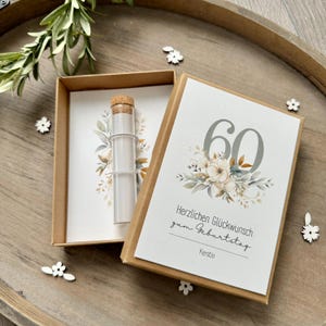 Könnte beinhalten: Eine braune Box mit einer weißen Karte darin. Die Karte hat ein florales Design mit der Zahl 60 in Grau. Der Text auf der Karte lautet "Herzlichen Glückwunsch zum Geburtstag Kerstin".