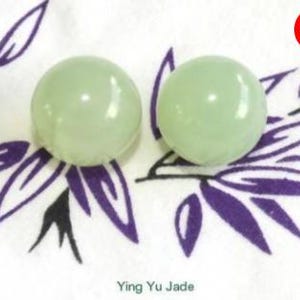 May include: Two pale green, round jade spheres. The spheres are on a white cloth with a purple leaf pattern. A red circle with the word "SALE" is in the upper right corner. The text "Ying Yu Jade" is at the bottom.