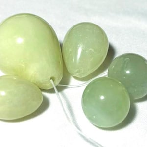 May include: Four smooth, polished jade eggs in various sizes and shapes. The eggs are light green and have a glossy finish.