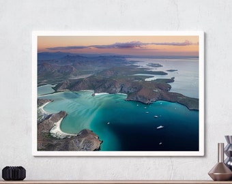 May include: An aerial photograph of a coastline with turquoise water, white sand beaches, and rocky islands. The sky is a soft pink and orange, suggesting a sunset or sunrise.