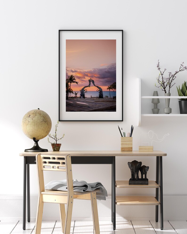 May include: A framed photograph of a sunset over the ocean with a large sculpture of two hands reaching towards each other in the foreground.
