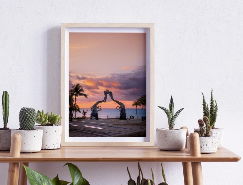 May include: A framed photograph of a sunset over the ocean with a large sculpture of two hands reaching towards each other in the foreground.