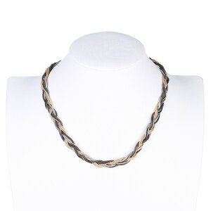 May include: A braided necklace with alternating strands of black, silver, and gold-toned metal. The necklace is displayed on a white mannequin bust, showcasing its woven design and color variations. This piece is a fashion accessory.