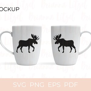 Puede incluir: Dos tazas blancas con siluetas negras de alces a cada lado. Las tazas est&aacute;n sobre un fondo blanco. El texto "MOCKUP" est&aacute; en la parte superior de la imagen. El texto "SVG PNG EPS PDF" est&aacute; en la parte inferior de la imagen.