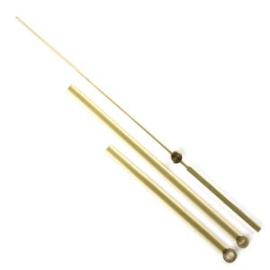 Puede incluir: Un conjunto de tres manecillas de reloj doradas, que incluyen las manecillas de las horas, los minutos y los segundos. Las manecillas son de metal brillante y están dispuestas en diagonal sobre un fondo blanco. Las manecillas de las horas y los minutos son tubulares.