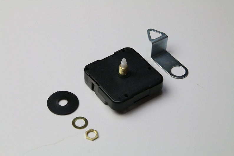 Puede incluir: Un movimiento de reloj negro con una perilla de pl&aacute;stico blanco, un soporte de metal, una arandela negra, una arandela dorada y una tuerca dorada.