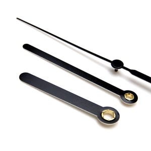 May include: Three black clock hands with gold accents. The hands are different lengths and are designed for a clock face.