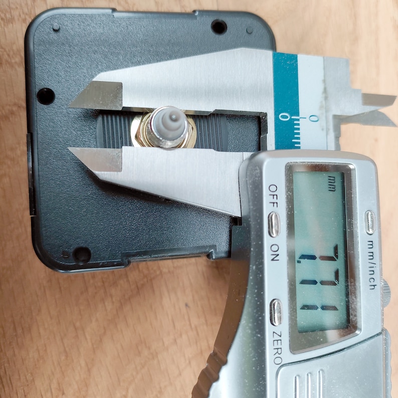 Puede incluir: Un calibre digital plateado mide un peque&ntilde;o mecanismo de reloj negro con una pieza de metal dorada. El calibre muestra 1,11 mm.