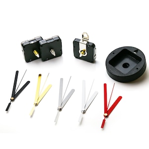 Puede incluir: Mecanismo de movimiento de reloj con engranajes de plástico negro y una aguja de metal plateado. El conjunto incluye una esfera de reloj de plástico negro, un juego de agujas de reloj negras, un juego de agujas de reloj doradas, un juego de agujas de reloj plateadas y un juego de agujas de reloj rojas.