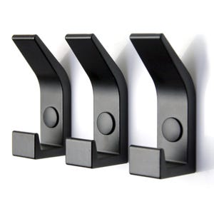 May include: Three black metal hooks mounted on a white wall. The hooks are curved and have a modern design.