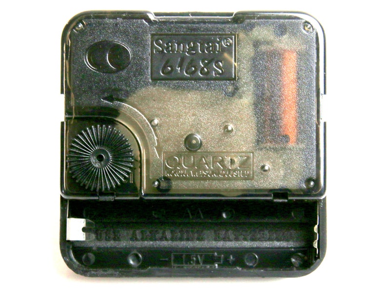 May include: A clear, rectangular quartz clock movement with the text "Sangtai 6468S" and "QUARTZ". The black plastic casing holds a battery and gears. The bottom reads "USE ALKALINE BATTERIES" and "1.5V".