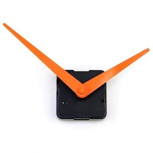 Puede incluir: Un mecanismo de reloj con manecillas de color naranja brillante y una base cuadrada negra. Las manecillas son largas y delgadas, y la base tiene un pequeño centro naranja. Las manecillas del reloj miden aproximadamente 15 cm de largo.