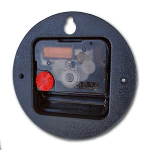 May include: Close-up of the back of a round clock mechanism. The clock is black with a clear plastic cover over the gears. The clock has a red knob and the text "QUARTZ 12 JEWELS UNADJUSTED PAT PEND 5000916" is visible.