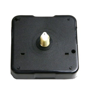 May include: A black square clock movement with a gold-colored threaded shaft and a white plastic tip. The clock mechanism has a textured surface and is designed for clock making and repair.
