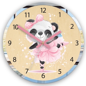 Może przedstawiać: Okrągły drewniany zegar z wzorem różowej baletnicy pandy. Tarcza zegara ma czarne cyfry i różową wskazówkę minutową. Panda ma na sobie różową baletnicę i różową kokardkę.