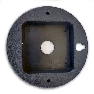 May include: A black round electrical box with a square opening and a hole in the centre. The box has a textured surface and a small hole on the side.