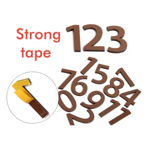 Op de afbeelding: Bruine schuimgetallen van 0 tot 9 en 1 tot 3 met sterk tape aan de achterkant. De getallen bevinden zich op een witte achtergrond.