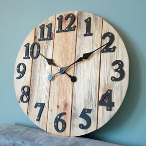 May include: A round wooden clock with black Roman numeral hour markers and black hands. The clock face is made of reclaimed wood planks.