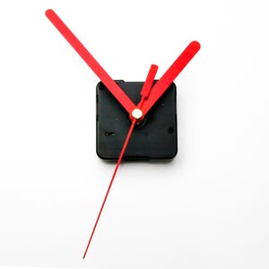 May include: Red clock hands with a black clock mechanism. The hands are attached to a black square clock mechanism.