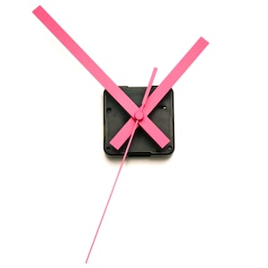 Op de afbeelding: Roze wijzers met een zwart uurwerkmechanisme. De wijzers zijn gekruist in de vorm van een 'X'.