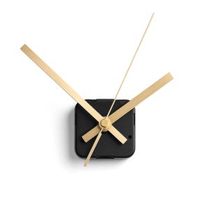 May include: A modern clock mechanism with a black square body and gold-colored hands. The hour and minute hands are wide and rectangular, while the second hand is thin and pointed. The clock hands are arranged at an angle against a white background.