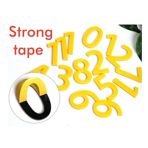 Może przedstawiać: Żółte numery z pianki od 0 do 9 z silną taśmą klejącą z tyłu. Tekst "Strong tape" jest napisany na czerwono.