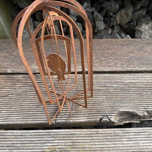 Könnte beinhalten: Ein rostiges Windspiel aus Metall mit einem Vogel-Silhouetten-Design. Das Windspiel besteht aus mehreren Metallschichten, die einen geschichteten Effekt erzeugen. Das Windspiel hängt an einer Holzoberfläche.