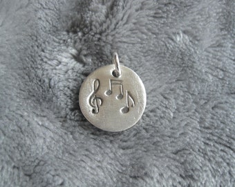 round silver pendant with embossed music notes and note key made of 999 silver, patinated