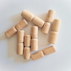 Könnte beinhalten: Ein Satz von acht Holzstiften, jeder mit einer Rille in der Mitte. Die Stifte sind sternförmig auf einer weißen Oberfläche angeordnet.