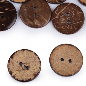 Könnte beinhalten: Eine Sammlung brauner Kokosnuss-Knöpfe mit jeweils zwei Löchern. Die Knöpfe sind in einem Halbkreis auf weißem Hintergrund angeordnet.