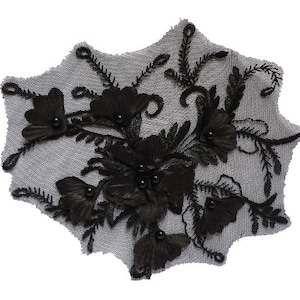 Könnte beinhalten: Schwarze florale Spitzenapplikation mit Perlenbesatz. Die Applikation zeigt mehrlagige Stoffblumen und Blätter mit kleinen schwarzen Perlen in der Mitte jeder Blume. Die Spitze hat einen gewellten Rand und ist vor einem hellgrauen Hintergrund angeordnet.