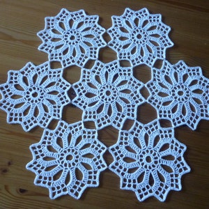 Könnte beinhalten: Weiße Häkeldeckchen mit Blumenmuster. Die Deckchen besteht aus sechs einzelnen Blumenmotiven, die miteinander verbunden sind.