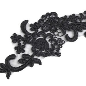 Könnte beinhalten: Schwarze Spitzenapplikation mit floralem Design. Die Spitze ist zart und filigran, mit verschiedenen Blumenformen und -größen. Die Applikation ist perfekt, um jedem Projekt einen Hauch von Eleganz zu verleihen.