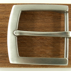 Könnte beinhalten: Eine silberne Gürtelschnalle aus Metall mit glatter, polierter Oberfläche. Die Schnalle ist rechteckig mit abgerundeten Ecken und hat ein schlichtes, klassisches Design.
