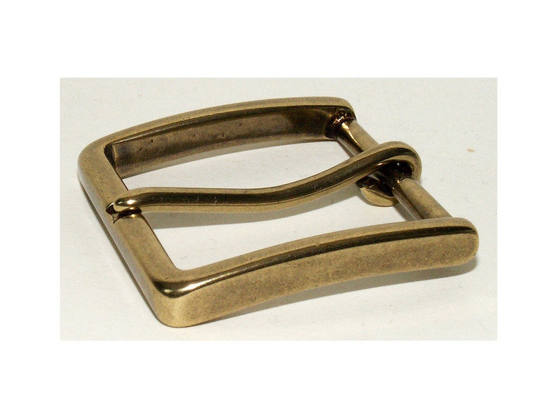 May include: A rectangular, antique brass belt buckle with a rounded bar and a single pin. The buckle has a slightly worn appearance, suggesting age or use. The metal has a warm, golden hue.