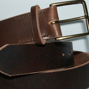 May include: A brown leather belt with a brass buckle. The belt is made of a dark brown leather and features a rectangular brass buckle. The leather has visible stitching and a classic design.