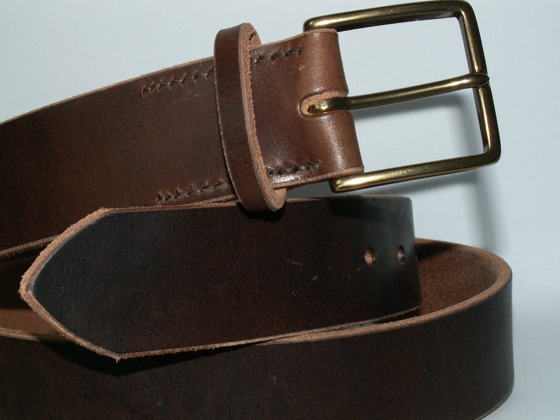 May include: A brown leather belt with a brass buckle. The belt is made of a dark brown leather and features a rectangular brass buckle. The leather has visible stitching and a classic design.