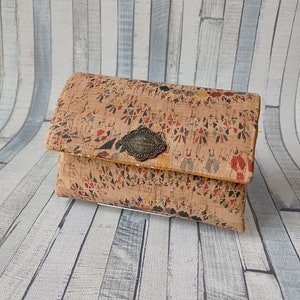 Può includere: Un piccolo portafoglio rettangolare in sughero con un motivo geometrico colorato. Il portafoglio ha una chiusura in metallo con le parole "Handmade with Love" incise.