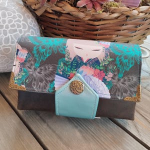 May include: A brown leather wallet with a colourful floral and butterfly design. The wallet has a turquoise flap with a gold button.