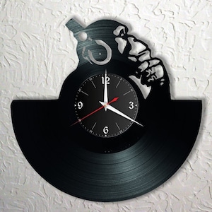 Può includere: Un orologio in vinile nero con la silhouette di una persona che tiene un microfono. Il quadrante dell'orologio è nero con numeri e lancette bianchi.