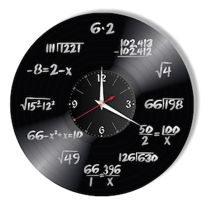 Op de afbeelding: Een zwarte vinyl platenspeler klok met witte wiskundige vergelijkingen en een zilveren wijzerplaat met zwarte wijzers. De vergelijkingen omvatten: 6.2, 1221, -8=2-x, √1521229, 102,413-102412, √4, 66/198, 66-x²+x=10, 50-100/2 X, √49, 126/630, 66_396/IX.