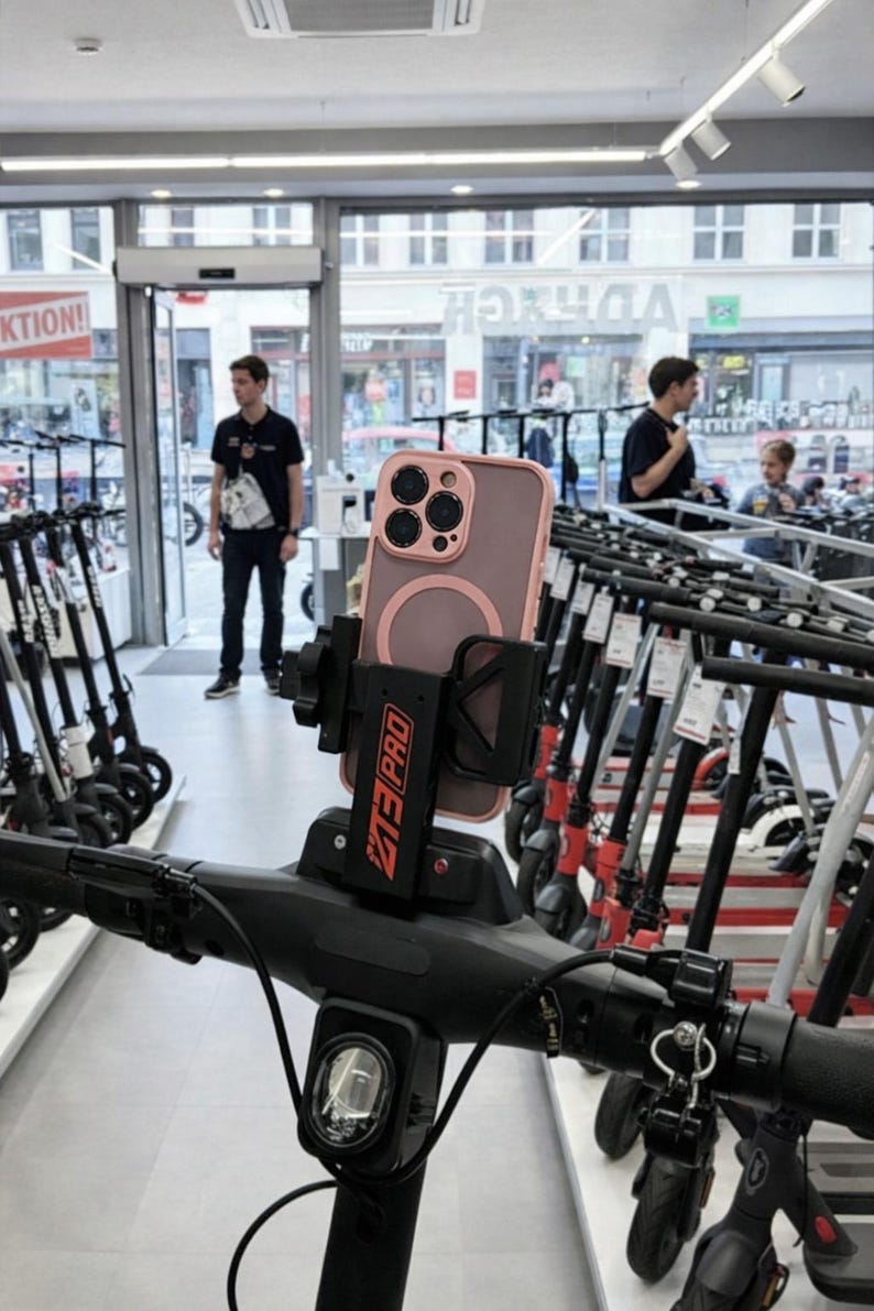 May include: A black scooter handlebar with a phone holder and a phone in a pink case. The phone holder has the text "MT3 PRO" in red. The background shows a store with scooters and people.