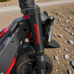 May include: Black and red electric scooter with the text "ZIP PRO" in red. The scooter has a black front fender, a headlight, and a rugged tire. The scooter is designed for off-road use.