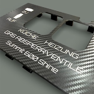 Puede incluir: Panel de fibra de carbono con letras blancas. El texto incluye "AUF", "ZU", "KÜCHE", "HEIZUNG", "GAS ABSPERRVENTILE" y "Summit 600 shine". El panel tiene secciones recortadas y pestañas de montaje.