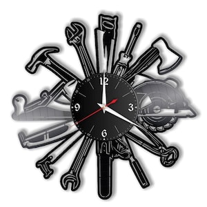 Puede incluir: Reloj de vinilo negro con una esfera negra y agujas blancas. El reloj está rodeado de varias herramientas, incluyendo un martillo, una llave inglesa, una sierra y un destornillador.