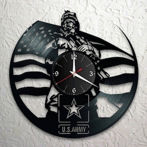 May include: Black vinyl record clock featuring a silhouette of a soldier standing in front of an American flag. The clock face is black with white numbers and hands. The soldier is holding a rifle and has a star on his chest. The text "U.S. ARMY" is printed below the star.
