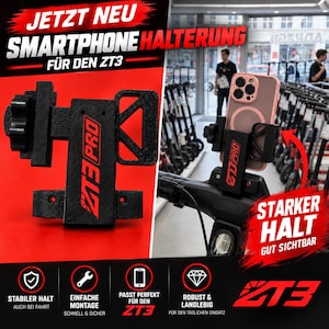 Może przedstawiać: Czarny uchwyt na smartfona do hulajnogi ZT3 o teksturowanym wykończeniu z czerwonym napisem ZT3 PRO. Urządzenie posiada regulowany mechanizm zaciskowy i jest pokazane zamontowane na kierownicy hulajnogi, trzymając różowy smartfon z magnetycznym pierścieniem.