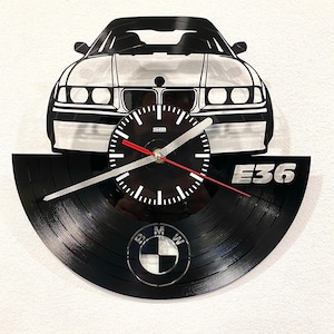 Puede incluir: Reloj de pared en blanco y negro con la silueta de un coche sobre una esfera. El reloj está hecho de un disco de vinilo e incluye el texto "E36" y el logotipo de BMW. Las manecillas son negras y blancas.