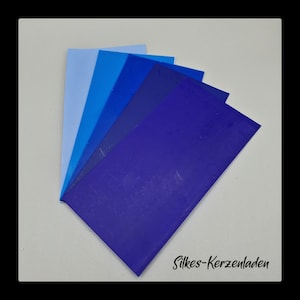 Könnte beinhalten: Sechs Blätter blauer Wachs in verschiedenen Farbtönen, von Hellblau bis Dunkelviolett, in Fächerform angeordnet. Die Blätter sind mit "Silkes-Kerzenladen" beschriftet.